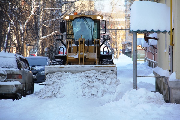 Водитель погрузчика осторожно сгребает снег в зауженном из-за оставленных машин дворе по ул. Шиловской, 7
